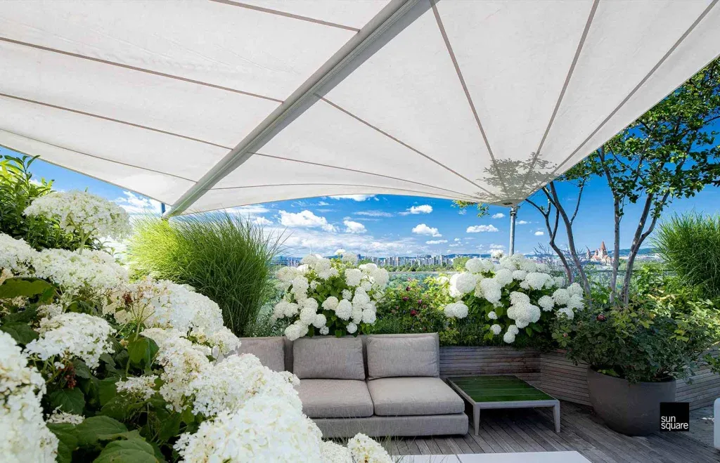 Weißes Sonnensegel über einer sonnigen Terrasse mit weißen Hortensien.